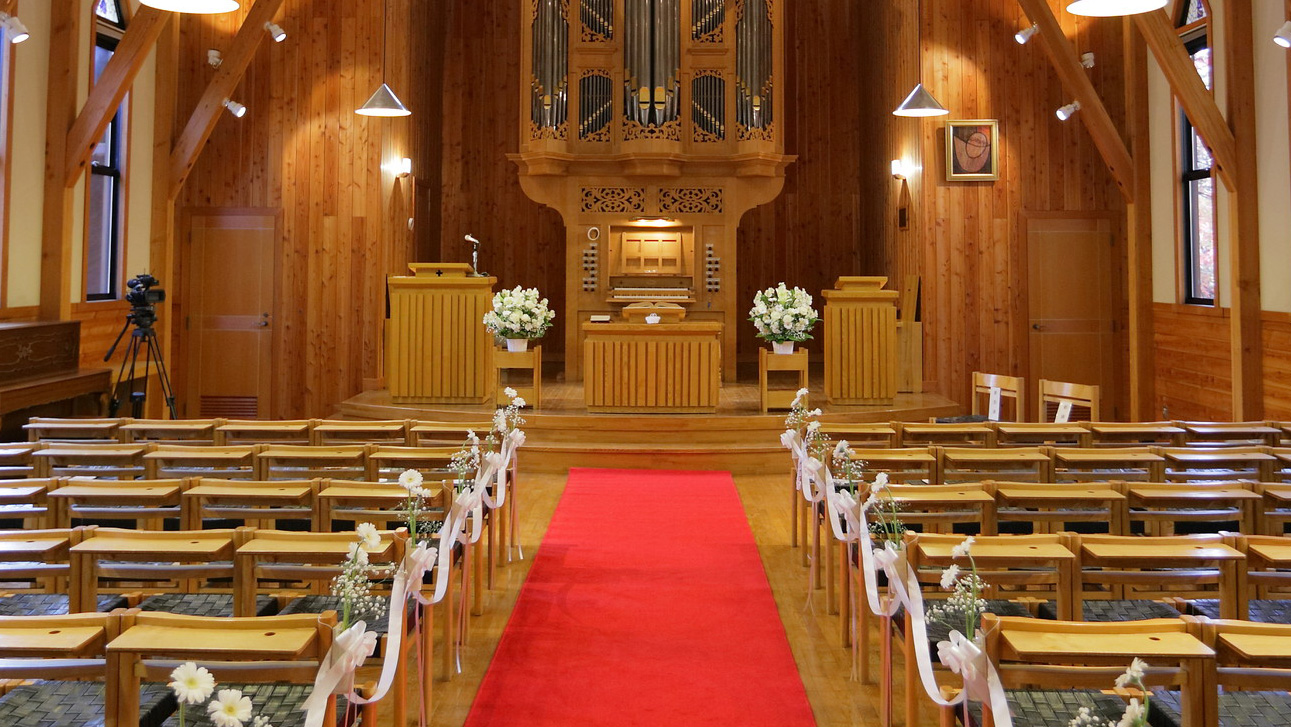 礼拝堂内の正面にパイプオルガンがあり中央通路に赤い絨毯が敷いてある写真